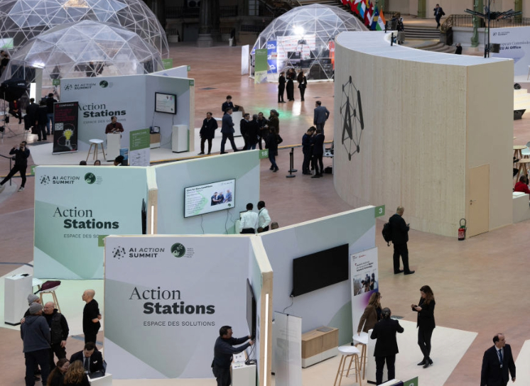 People interact at various booths and displays in a large indoor event space with geodesic domes and flags in the background.