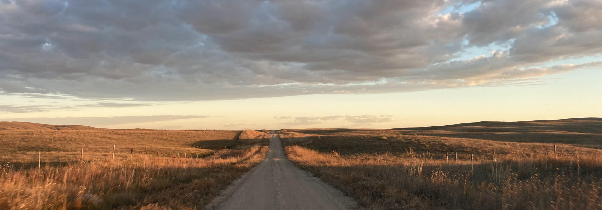 A dirt road through a rural landscape at sunset with cloudy skies.